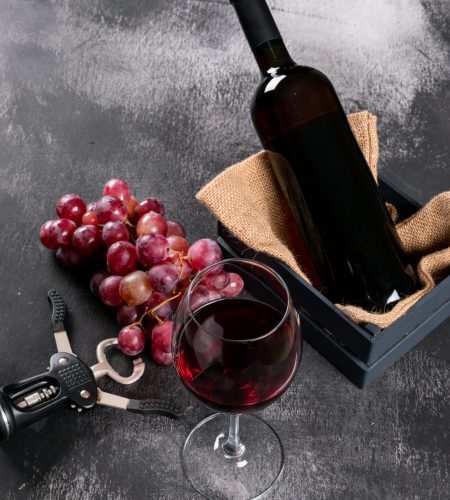 vista-lateral-vino-tinto-con-uva-en-caja-con-tela-de-saco-en-piedra-negra-vertical